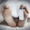 Close-up of the feet of a corpse covered in a sheet; with a blank tag tied on the big toe of the left foot; with an added vignette and copy space