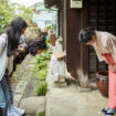 Mature landlady greeting young female guests at ryokan. Women are bowing in front of inn owner. They are standing outside hotel.