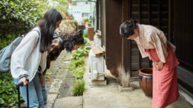 Mature landlady greeting young female guests at ryokan. Women are bowing in front of inn owner. They are standing outside hotel.