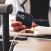 Cropped image of a South Asian man waiting in airport lounge charging his phone using power bank before departure. Focus on the foreground.