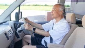 An older man is driving a car with his hands on the wheel. He is smiling and he is enjoying the ride