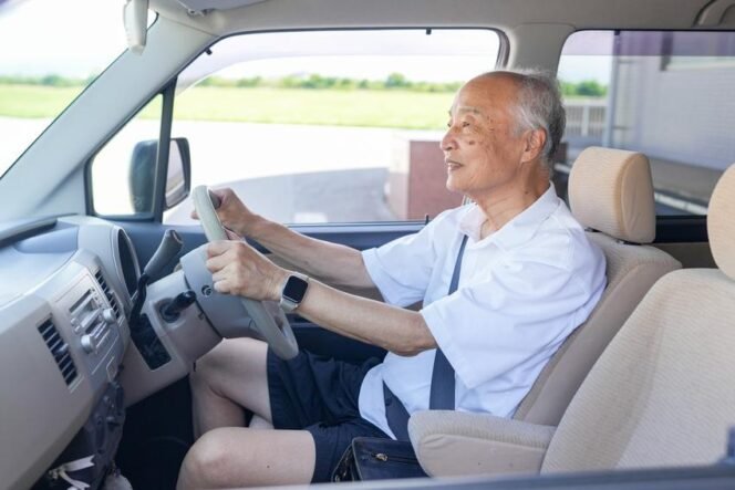 
					An older man is driving a car with his hands on the wheel. He is smiling and he is enjoying the ride